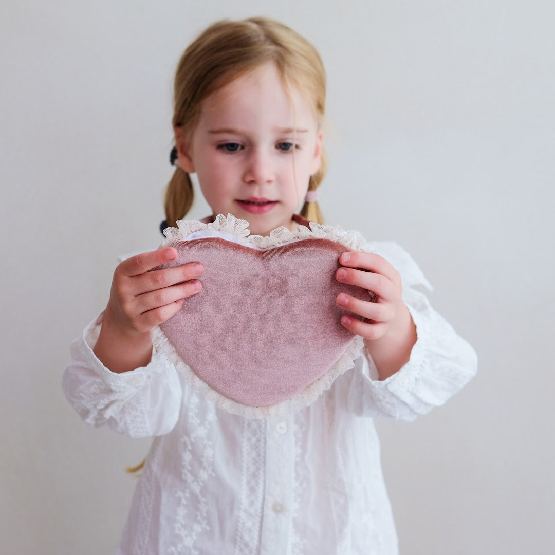Meisje houdt een roze fluwelen hartvormig schoudertasje met beide handen vast.