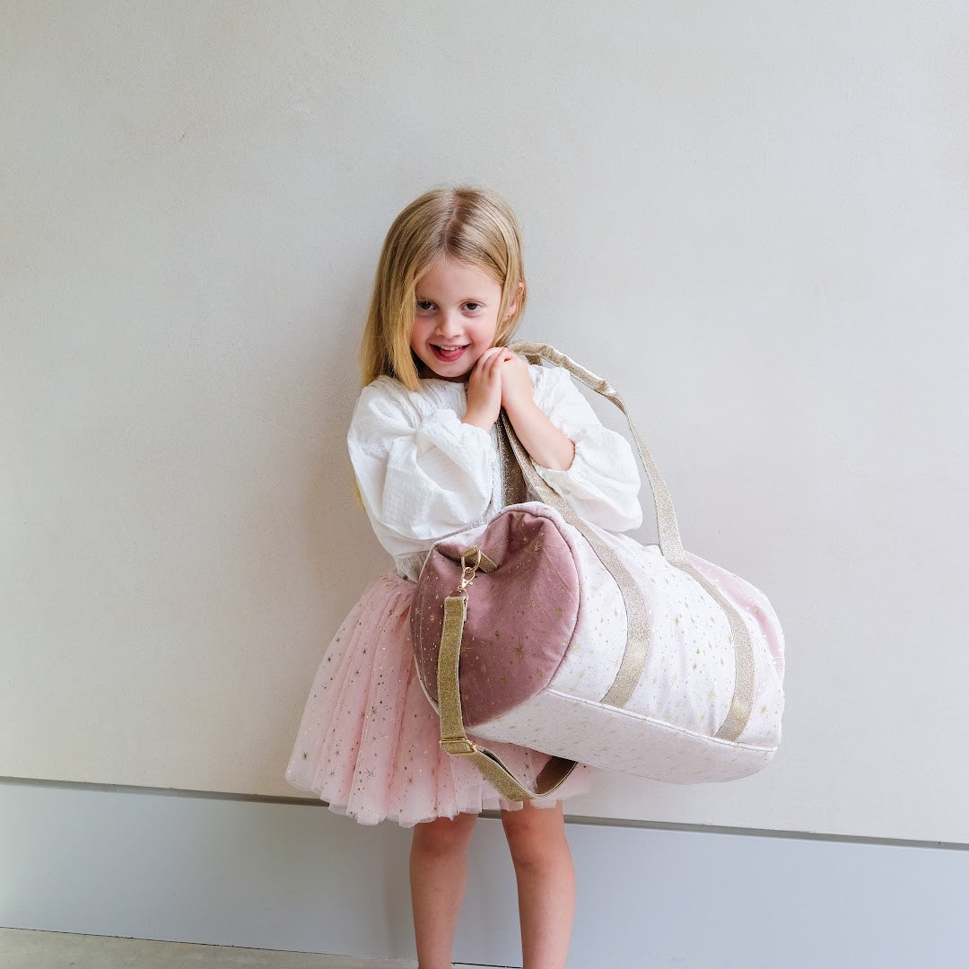 Een lachend meisje draagt de mimi & lula roze weekendtas met sterren over haar schouder.