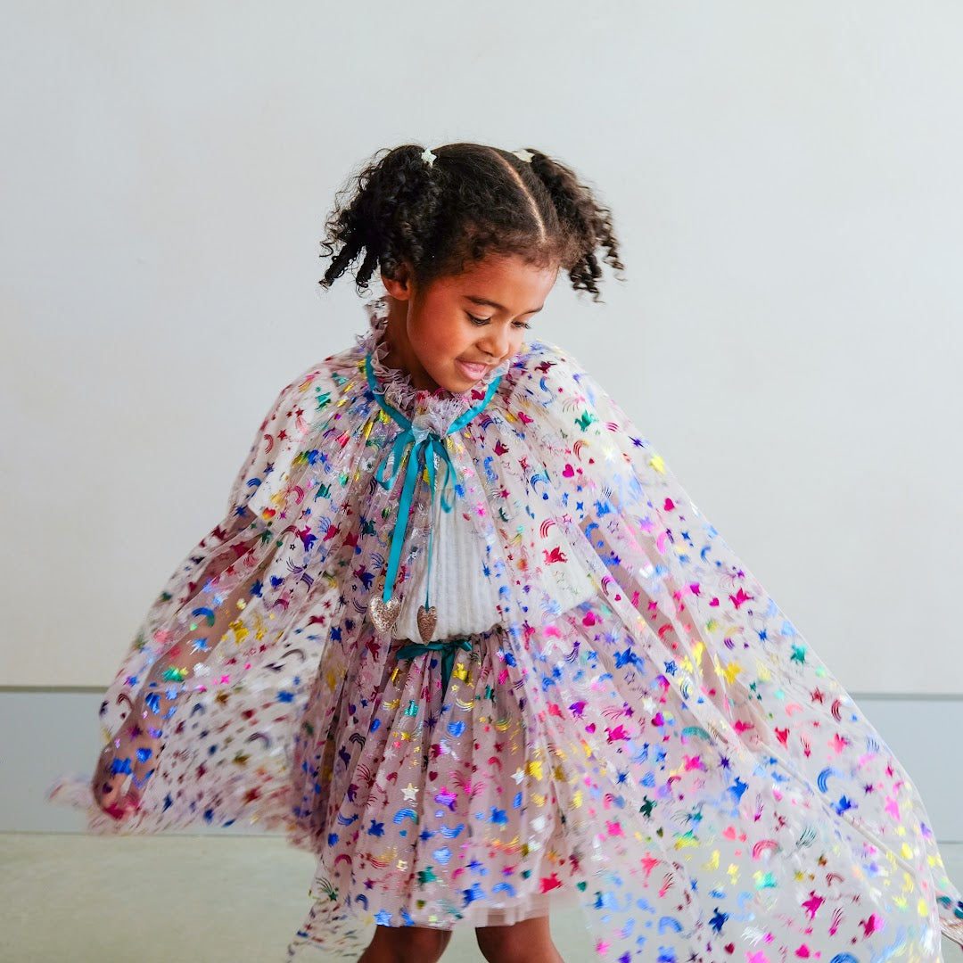Een meisje draagt de Mimi & Lula verkleedcape met regenboog eenhoorn motief, de cape wijd uitgespreid.
