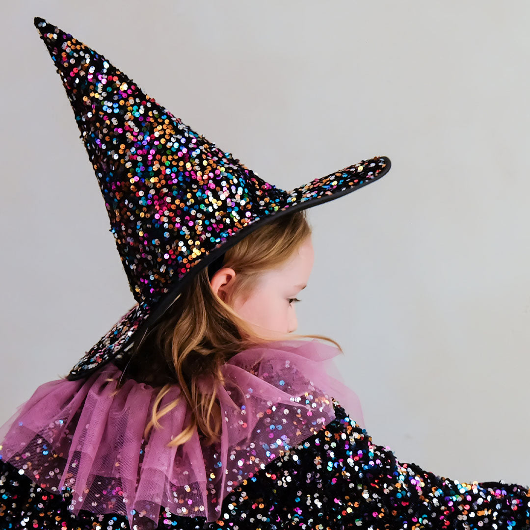 Kind draagt een mimi & lula heksenhoed en cape met veelkleurige pailletten, van achteren gezien.