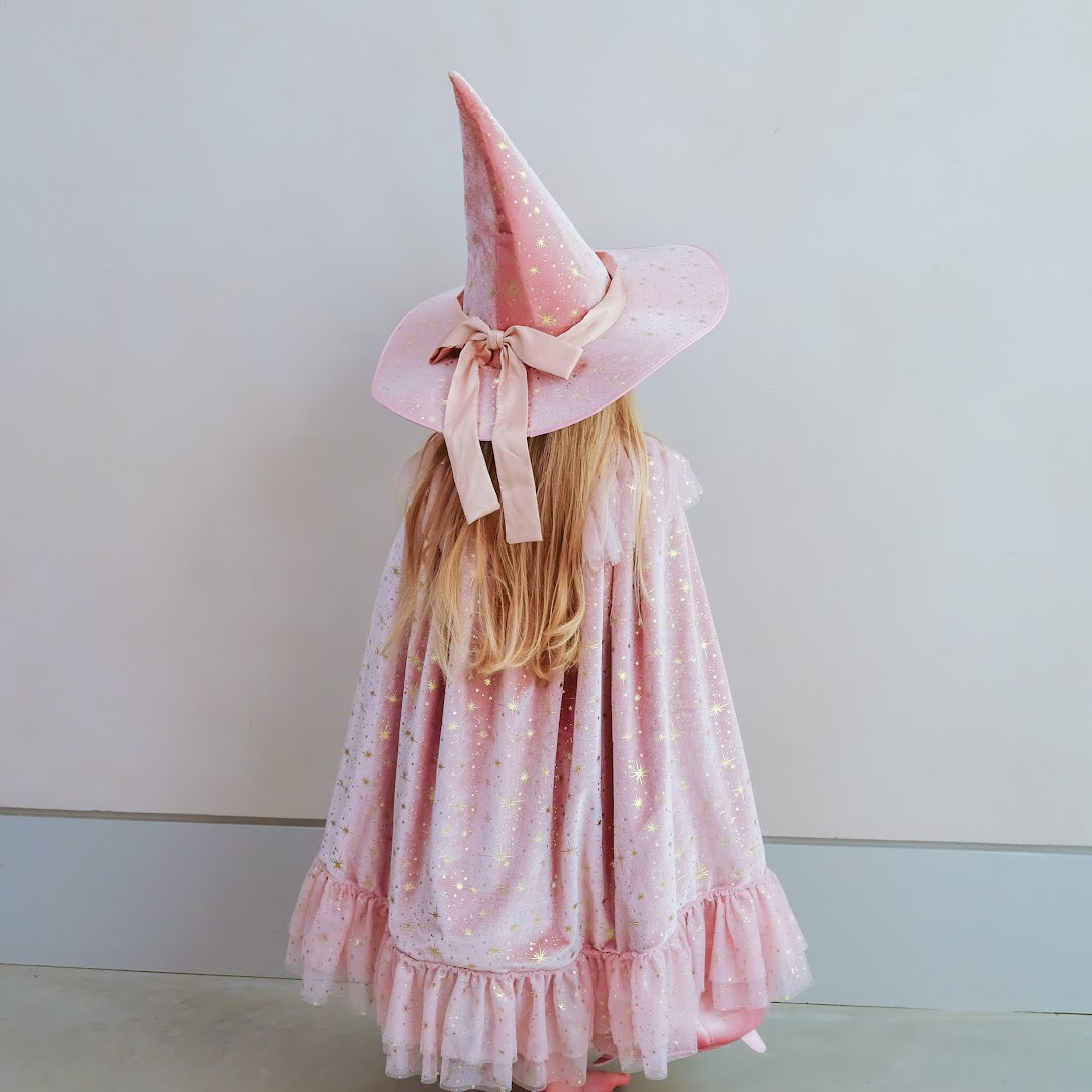 Kind van achteren gezien, draagt de roze verkleedcape met sterren en een bijpassende roze heksenhoed.