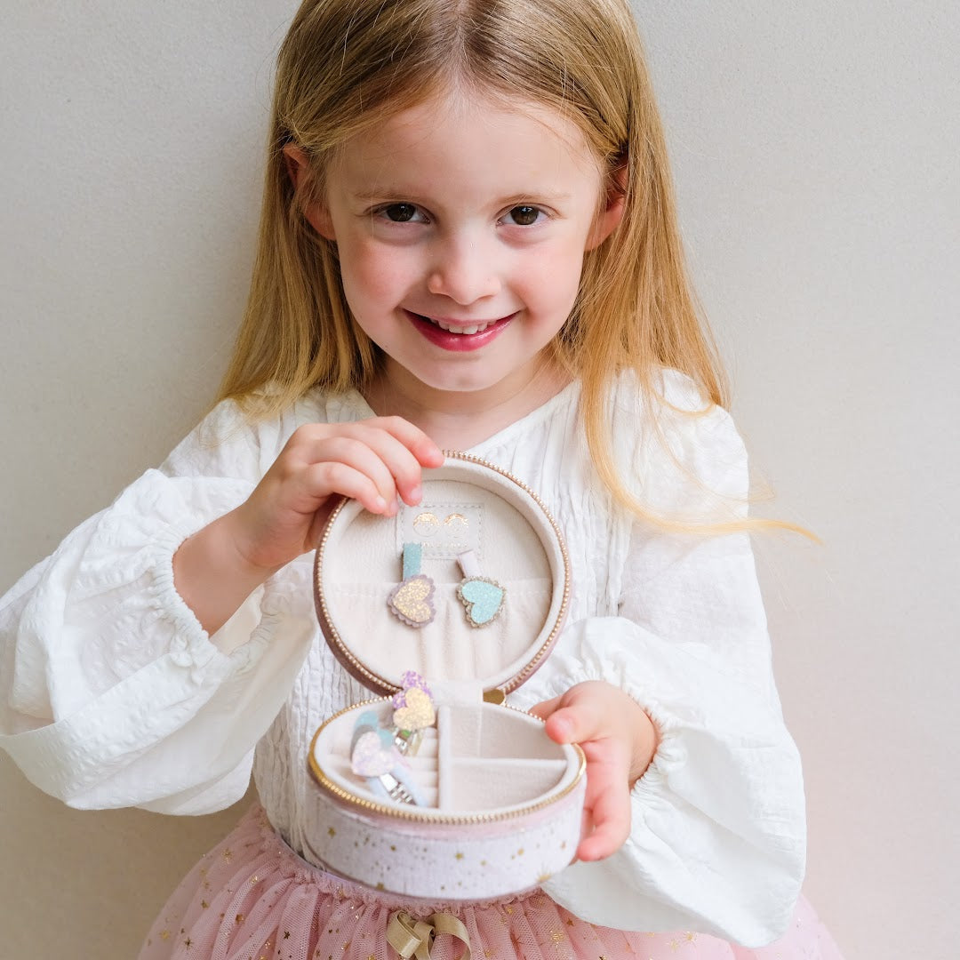 Een lachend meisje toont het open Mimi & Lula roze sieradendoosje met sieraden erin.
