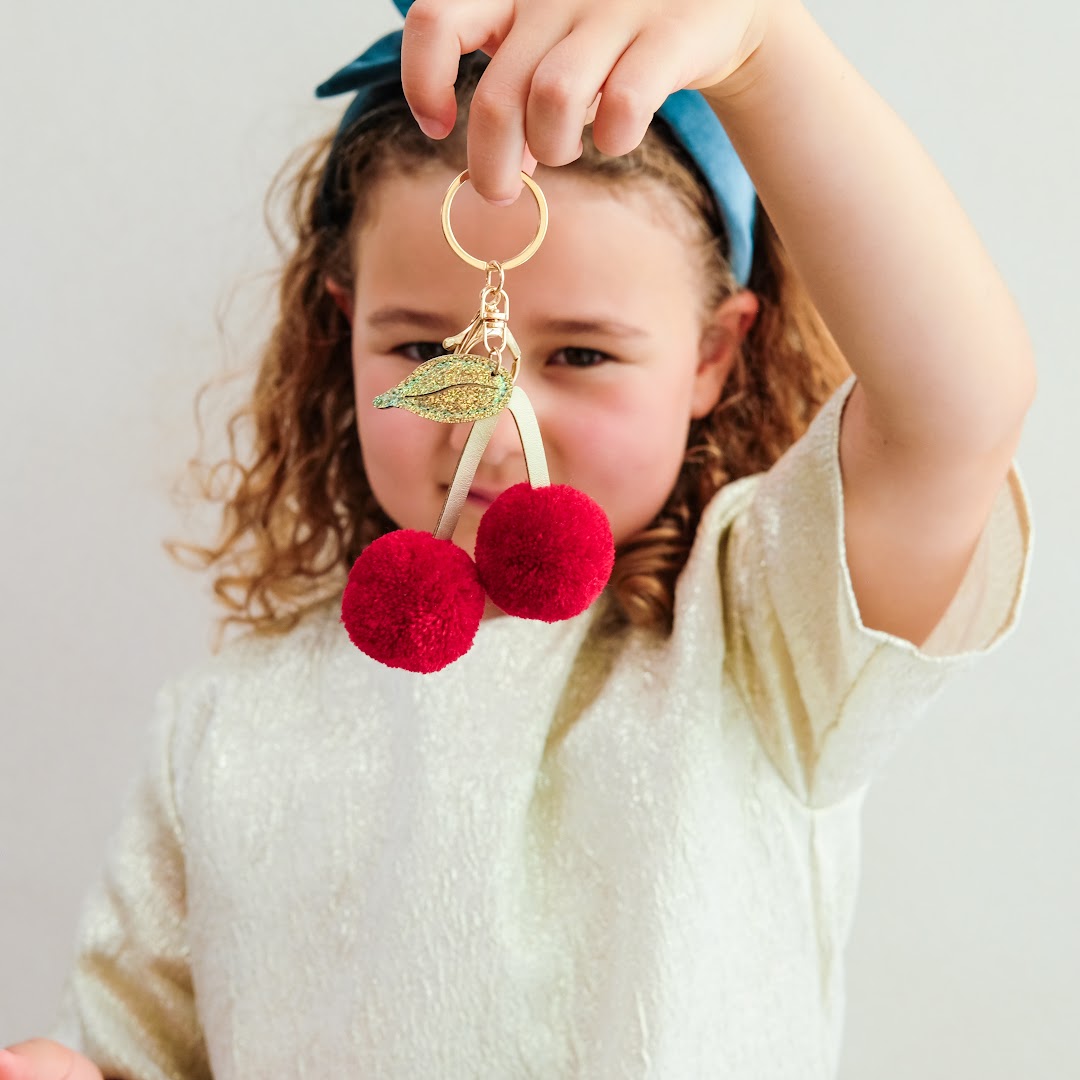Een kind houdt de Mimi & Lula sleutelhanger met rode pompon kersen omhoog.