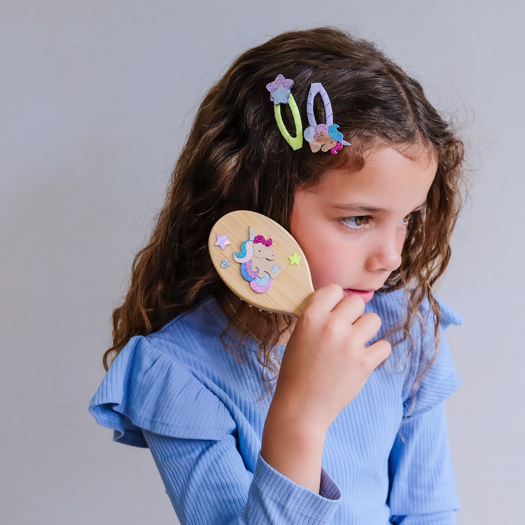 Meisje met lang krullend haar borstelt haar haar met de mimi & lula houten eenhoorn haarborstel.