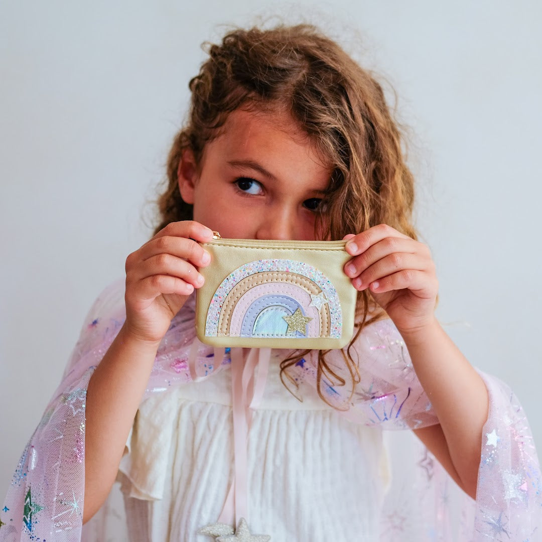 Een kind houdt de gouden kinderportemonnee met regenboog en sterren voor haar gezicht.