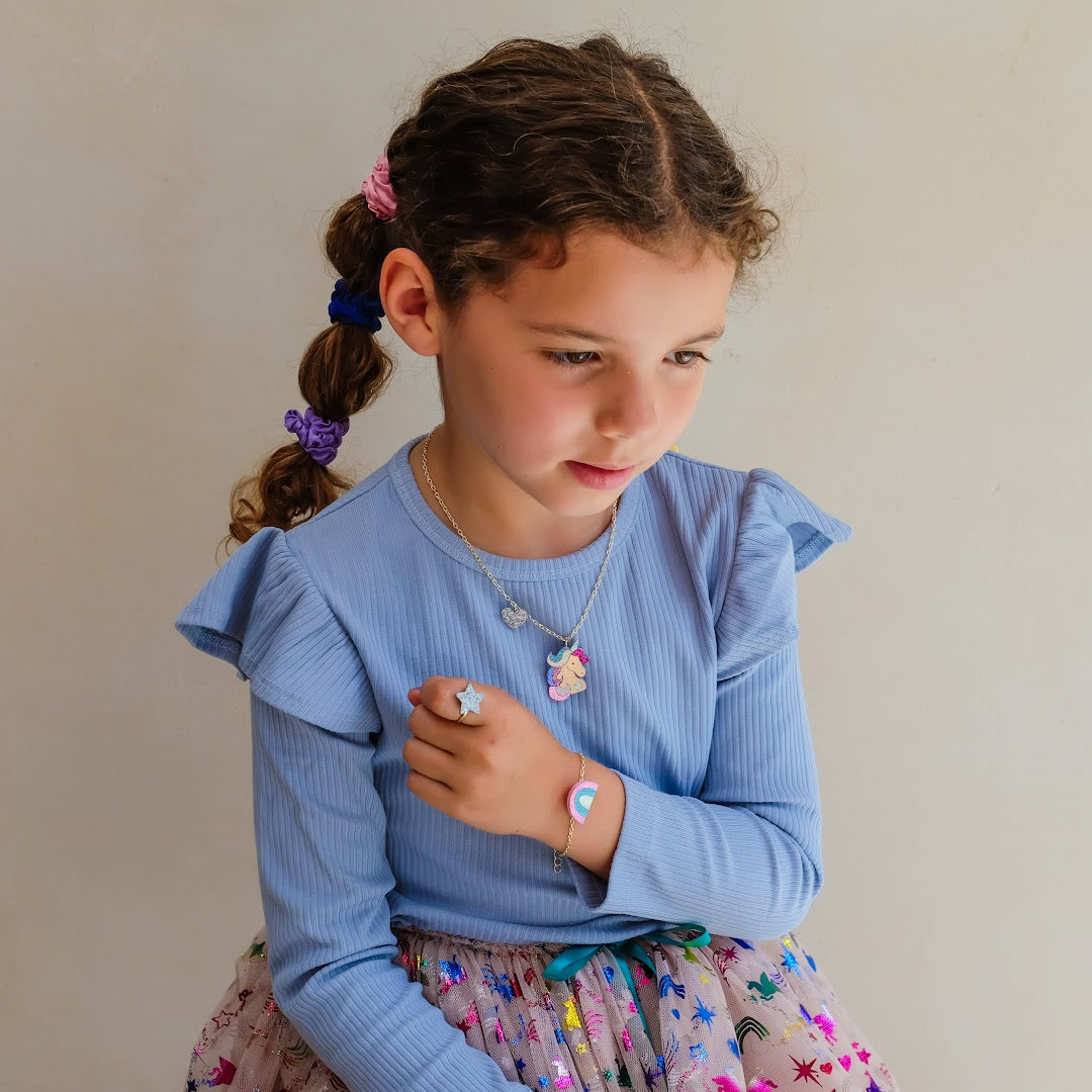 Een meisje draagt de mimi & lula kinder sieradenset met een eenhoorn ketting, sterrenring en regenboog armband.