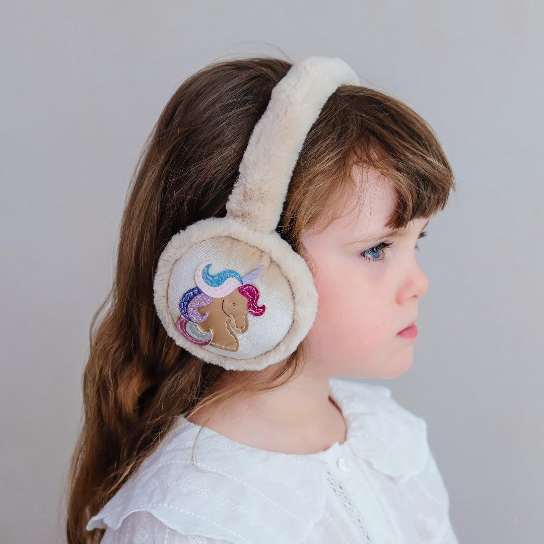 Een kind met lang bruin haar draagt de mimi & lula beige eenhoorn oorwarmers.