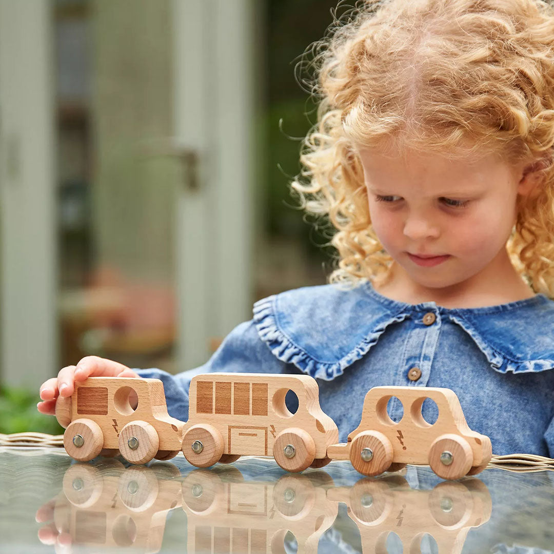 Een jong meisje speelt buiten met de drie tickit houten speelgoedvoertuigen die aan elkaar gekoppeld zijn.