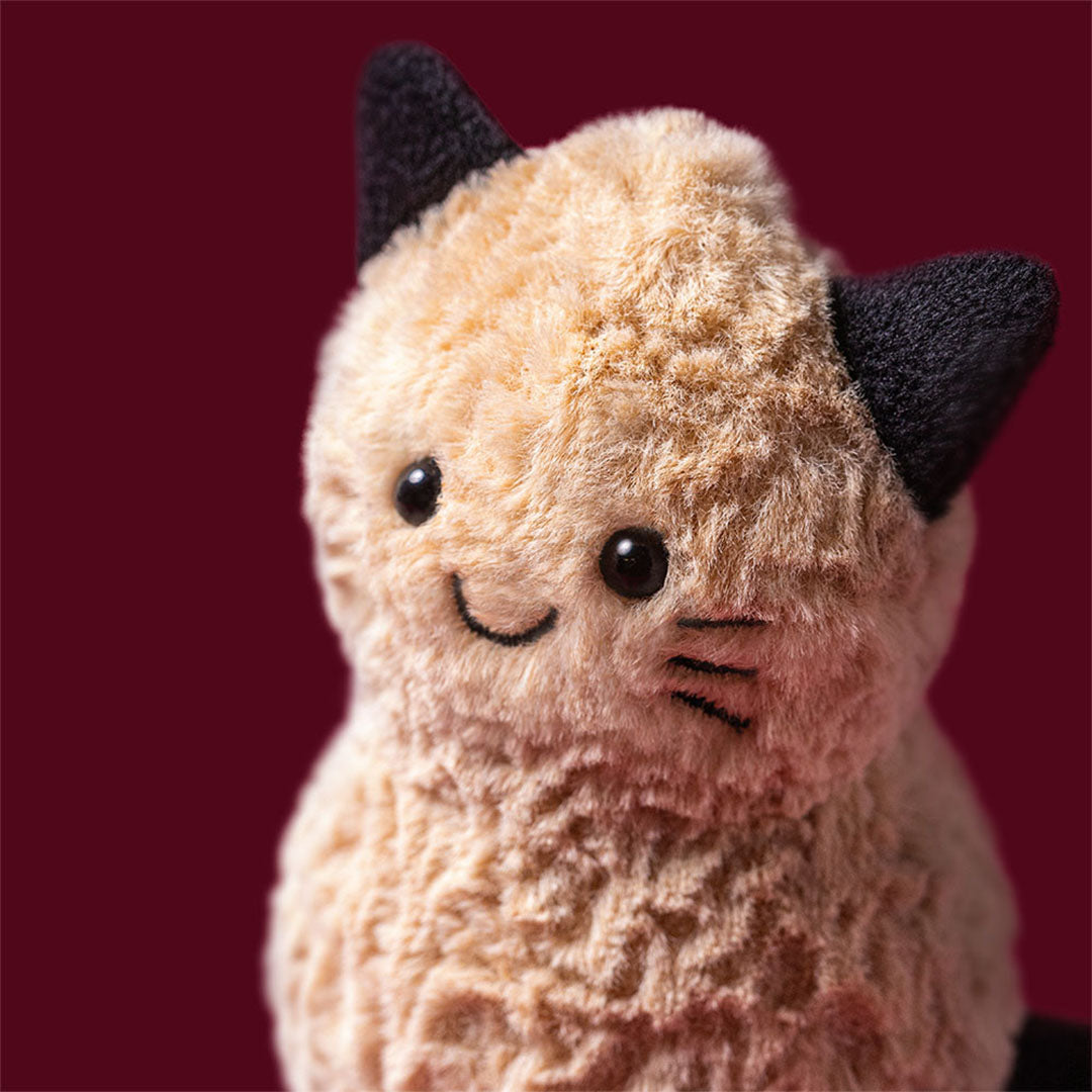 Detailopname van de kop van de Jellycat pluchen pinda kat knuffel, met geborduurde ogen en snorharen.