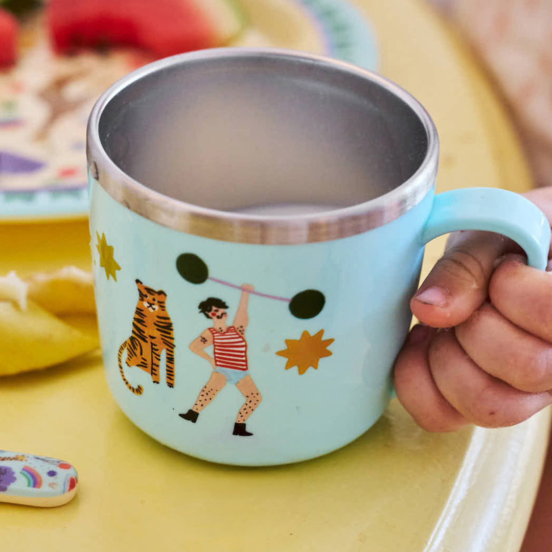 Een kinderhand houdt de Rice kinderbeker met een tijger en sterke man illustratie vast.