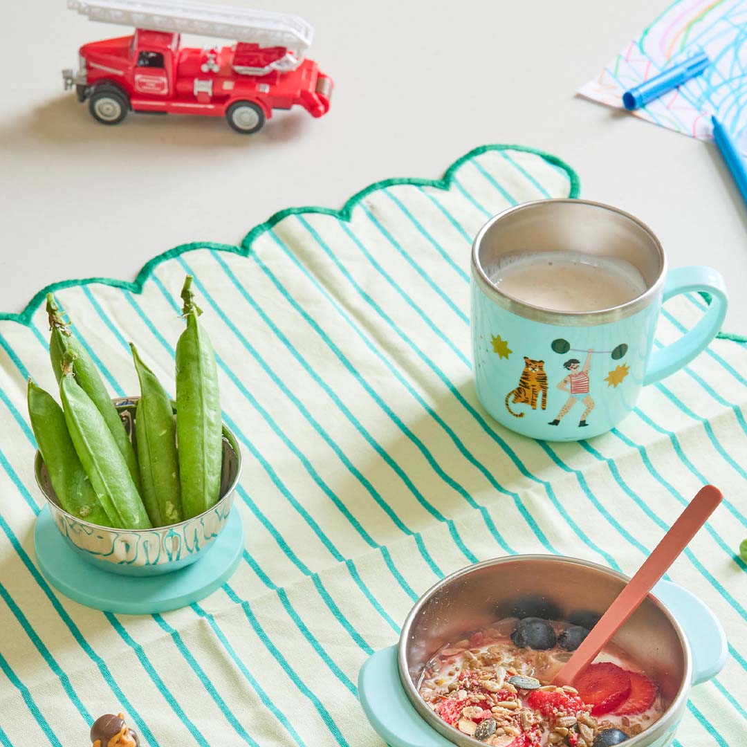 Een ontbijttafel met de Rice kinderbeker met tijger en sterke man, een kom erwten en ontbijtgranen.