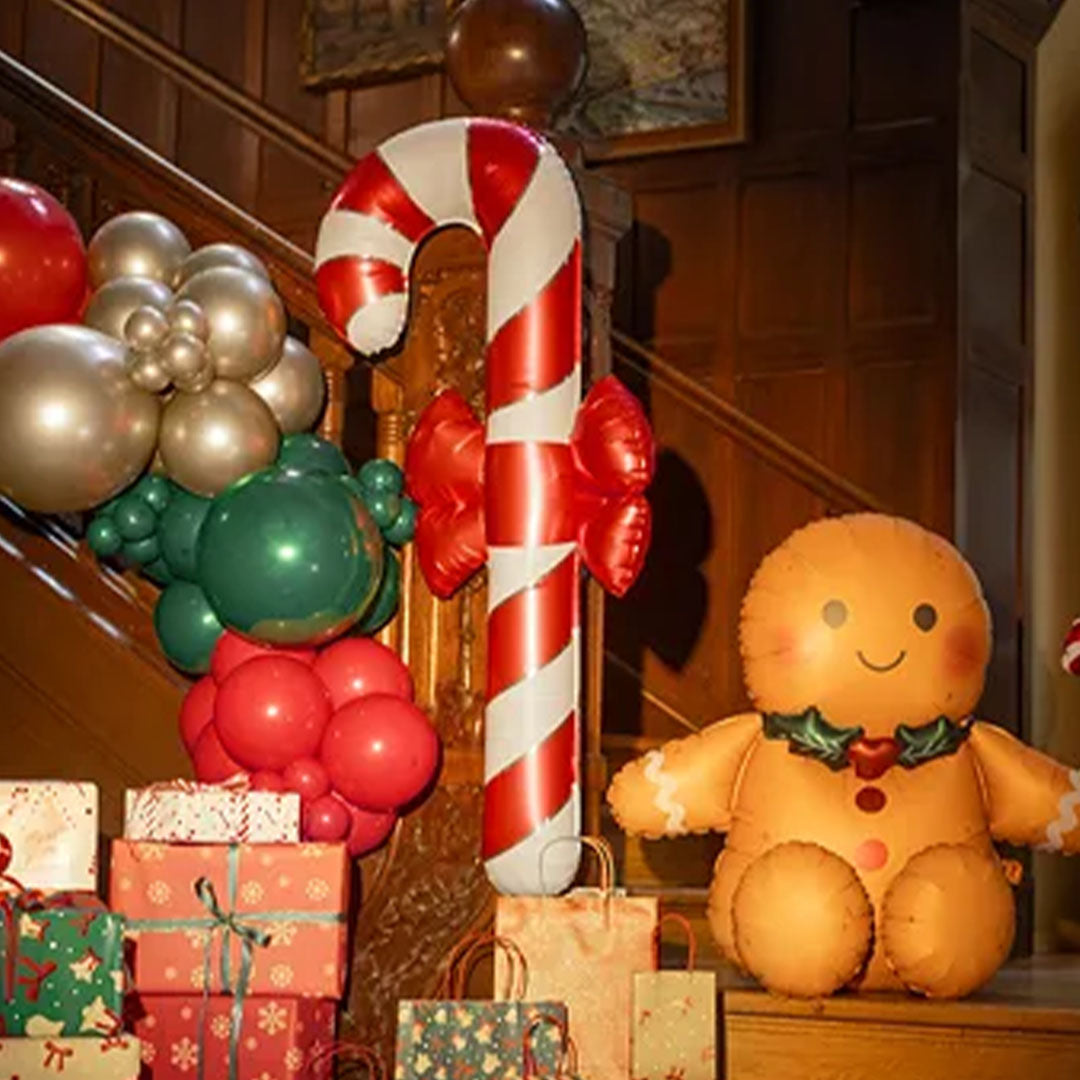 De partydeco zuurstok folieballon staat als kerstdecoratie tussen andere ballonnen en cadeaus bij een trap.