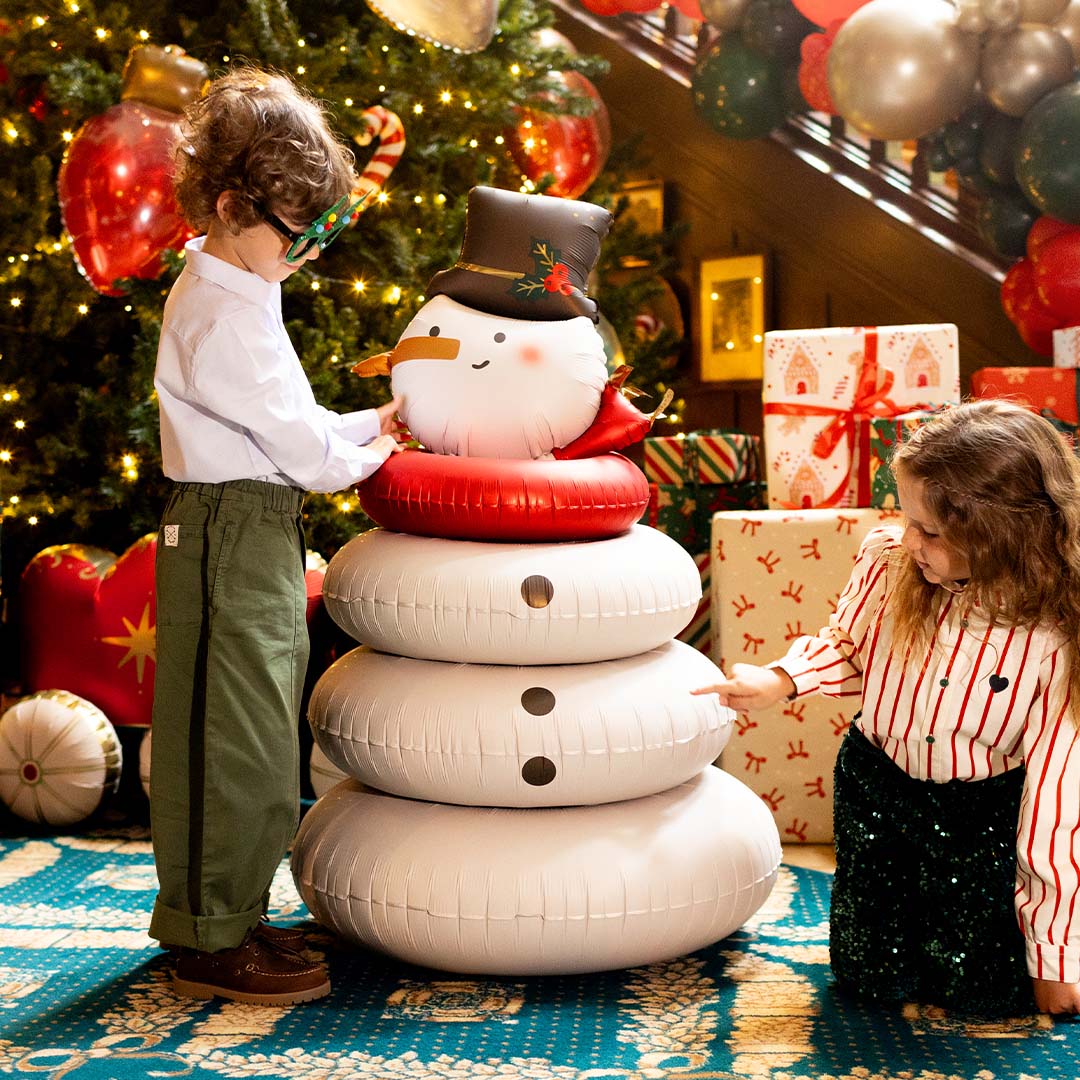 Twee kinderen spelen met de Partydeco folieballon sneeuwpop in een kerstversierde kamer.