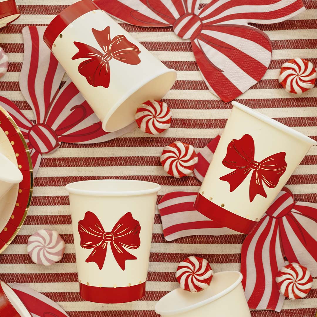 Partydeco papieren bekers met rode strikken op een rood-wit gestreepte ondergrond met decoraties.