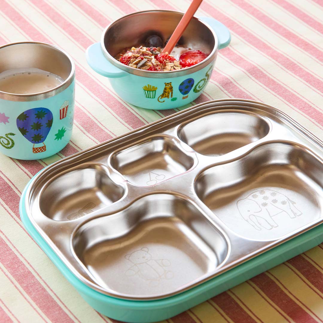 rice RVS vakjesbord met mintgroene onderkant en circusfiguren, naast een bijpassende kom en beker.