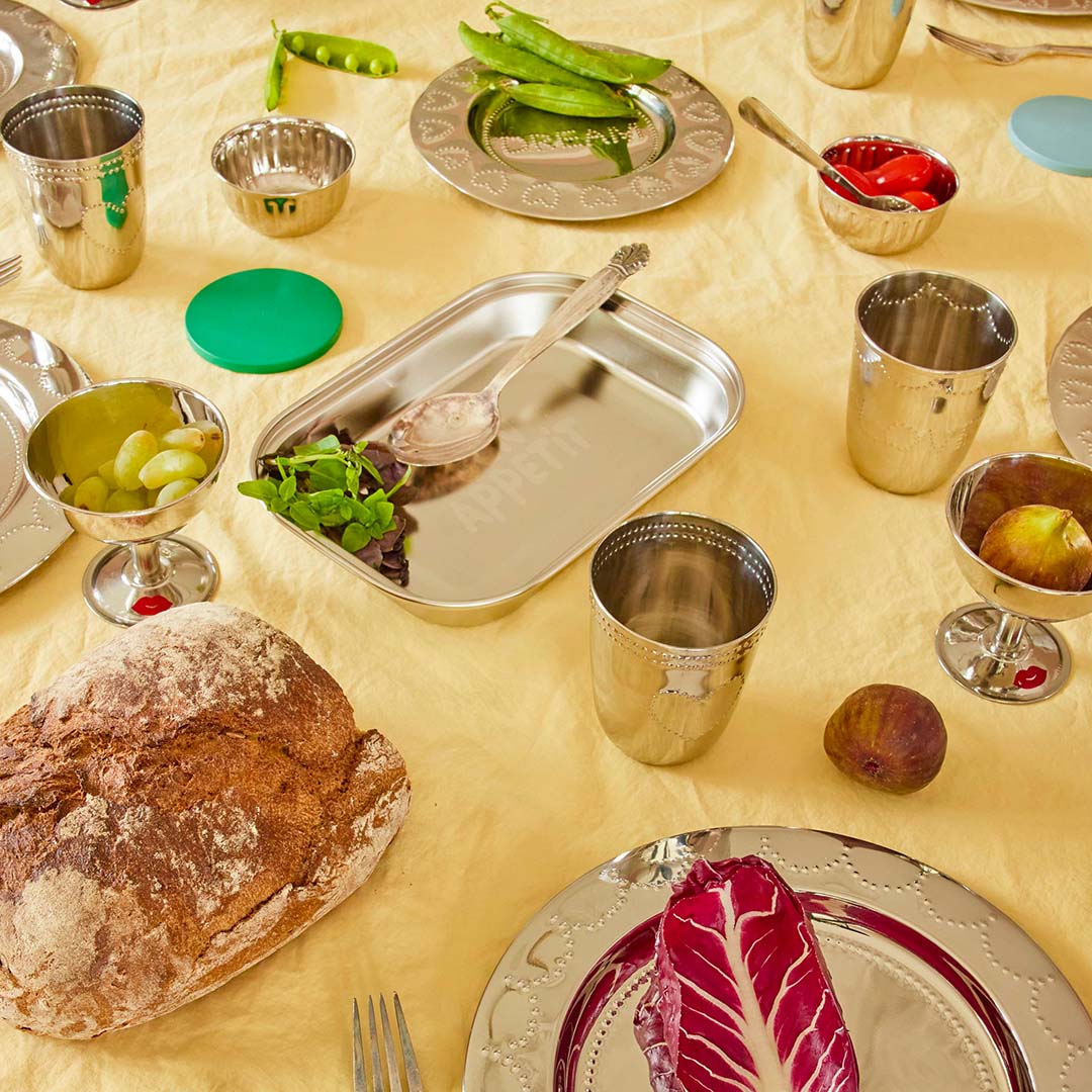 Een gedekte tafel met diverse zilverkleurige serviesstukken, waaronder een rice rvs vakjesbord met de tekst 'Appetit'.