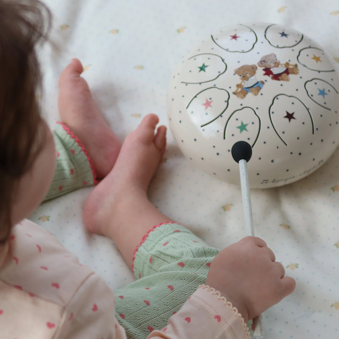 Een baby speelt met de Konges Sløjd houten tongtrommel met teddybeer- en sterrenpatroon.