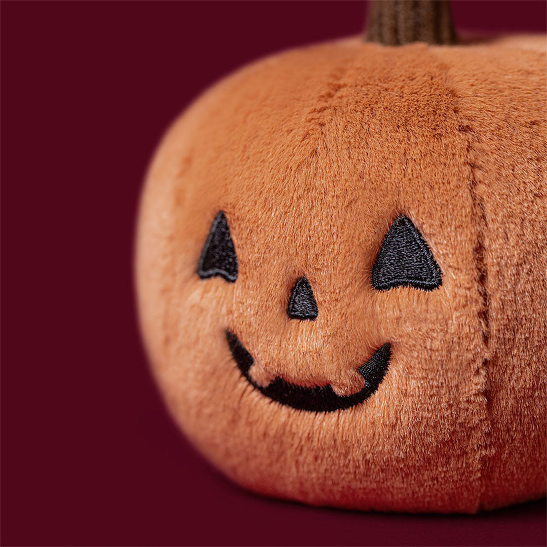 Detail van de Jellycat pluchen Halloween pompoen knuffel met geborduurd Jack-o'-lantern gezicht.