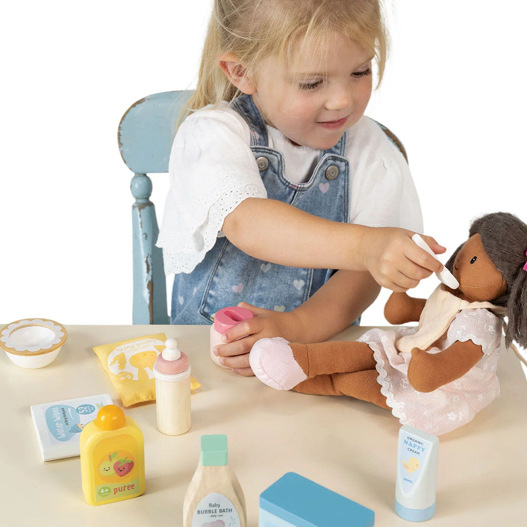 Een meisje voedt een pop met een lepel uit de Tender Leaf Toys poppenverzorgingsset op een tafel.