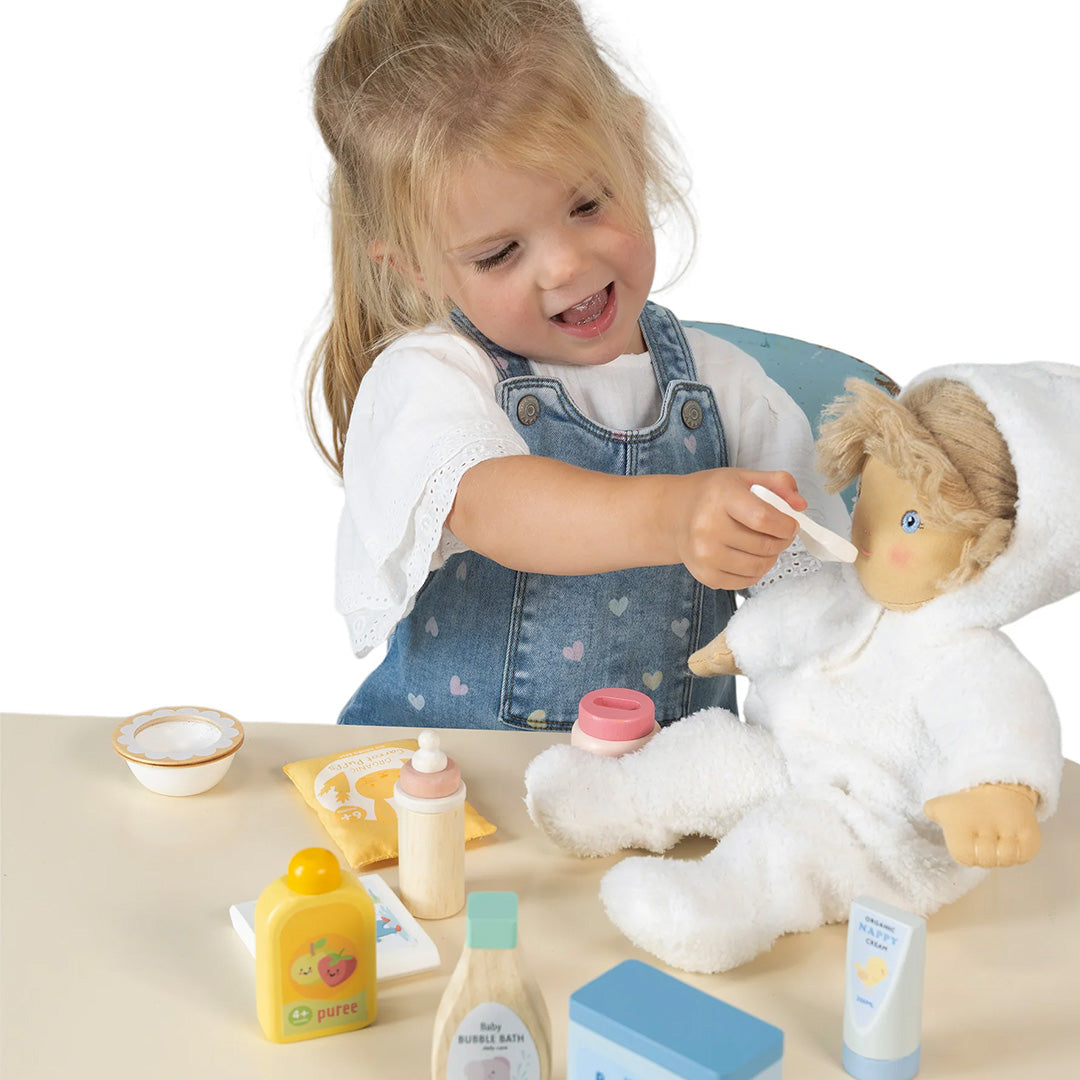 Een lachend meisje voedt een pop met een lepel uit de Tender Leaf Toys poppenverzorgingsset.