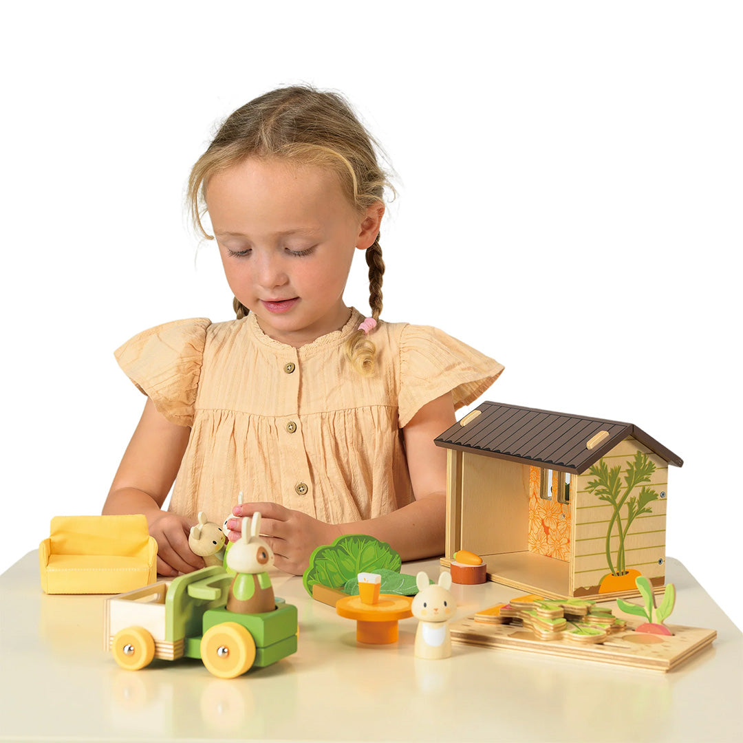 Een meisje met vlechten speelt geconcentreerd met de Tender Leaf Toys konijnen moestuin speelset.
