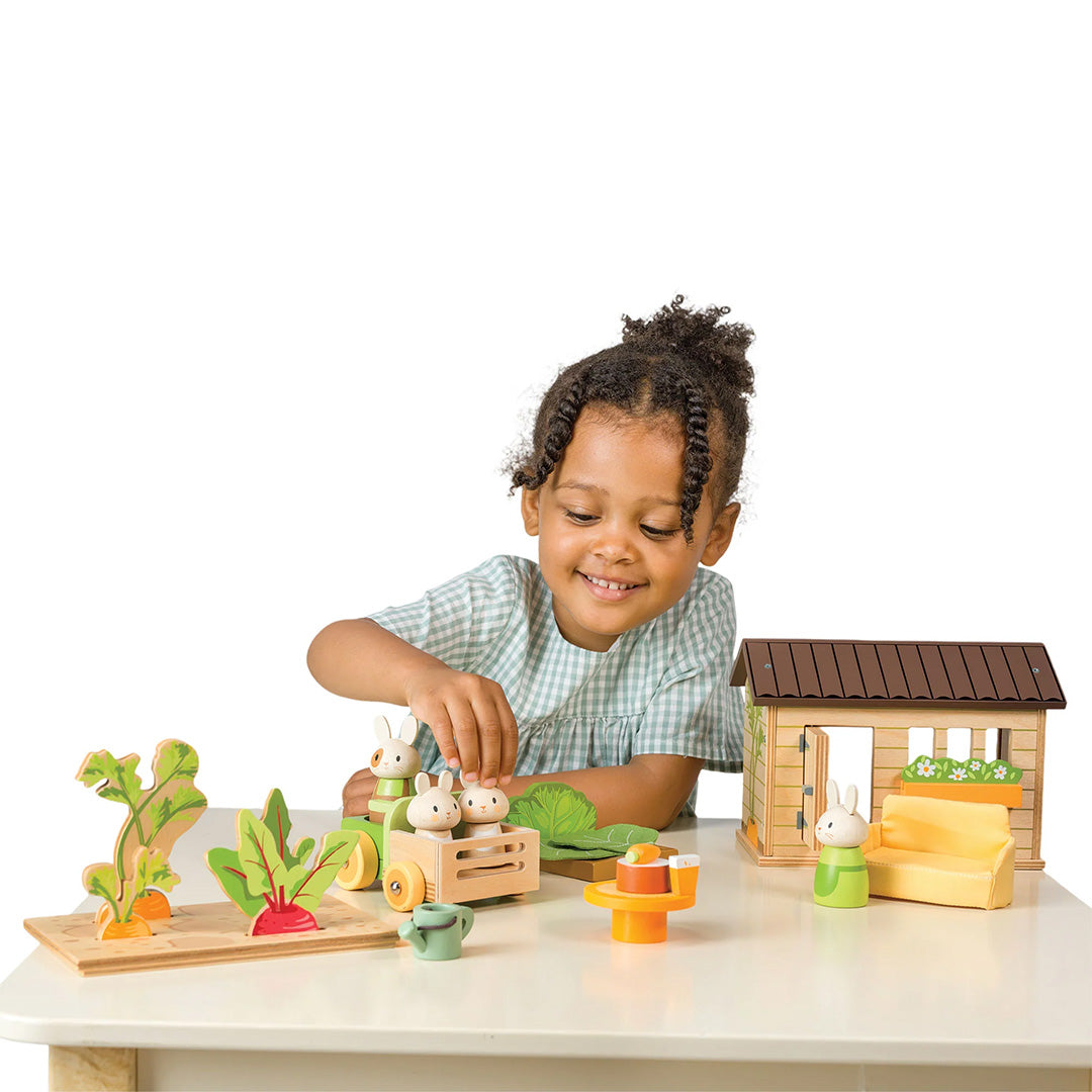 Een lachend meisje speelt met de Tender Leaf Toys konijnen moestuin speelset op een witte tafel.