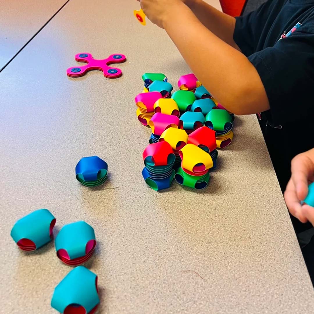 Een kind bouwt met kleurrijke Clixo magnetische bouwstukken op een tafel.