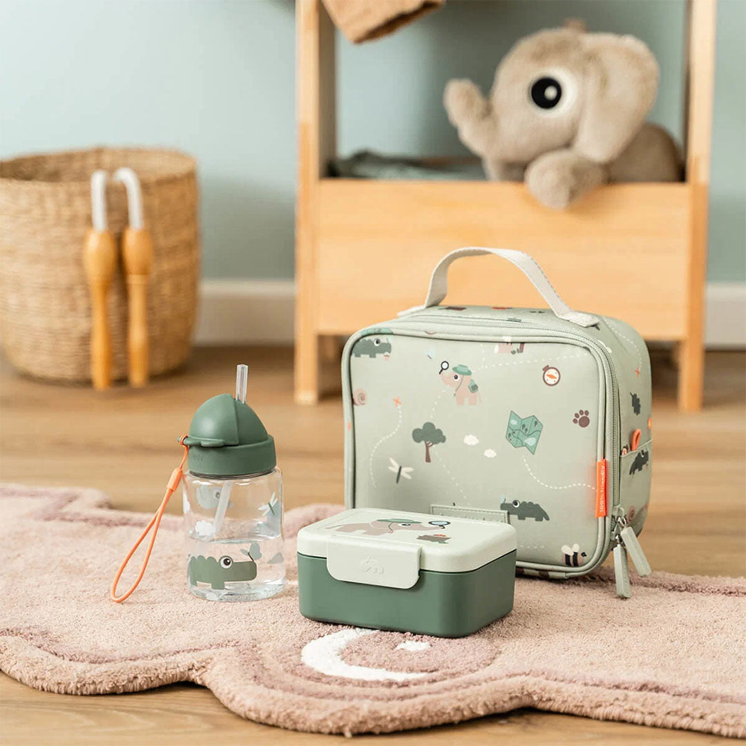 De groene kinder lunchtas met dierenpatroon, een bijpassende lunchbox en drinkfles staan op een roze vloerkleed.