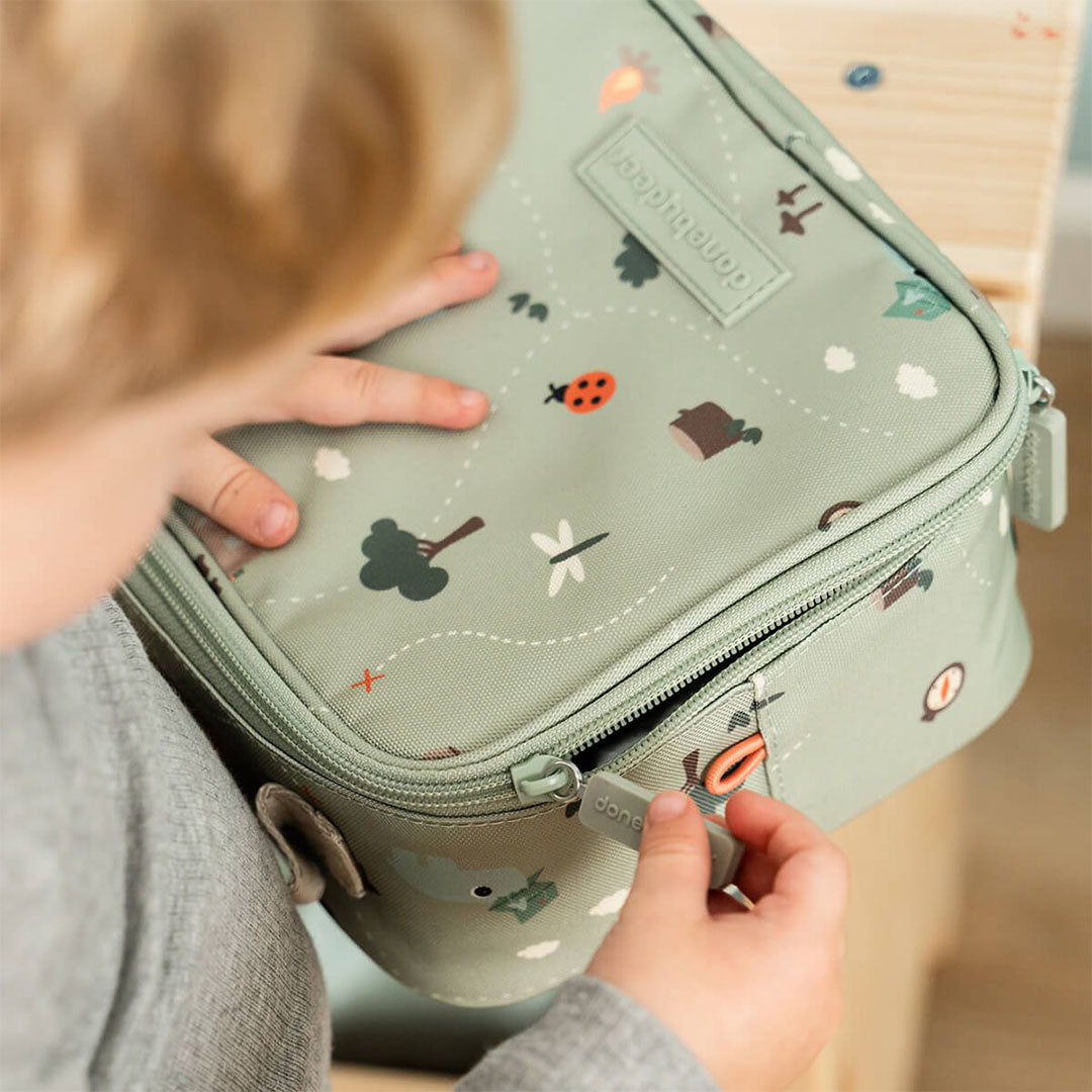 Een kind sluit de groene kinder lunchtas met het Tiny Trails dierenpatroon.