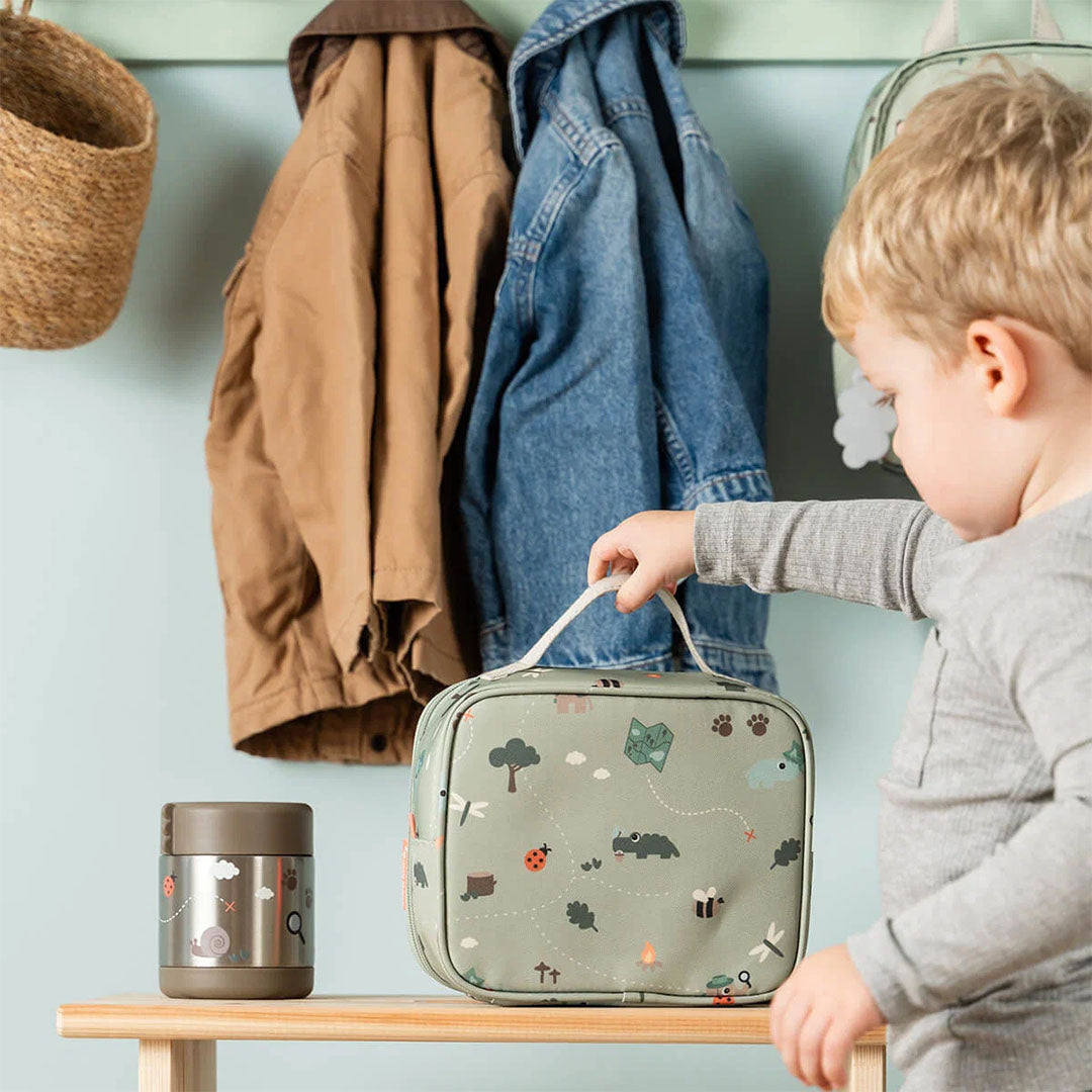 Een kind pakt de groene kinder lunchtas met dierenpatroon van een houten bankje.
