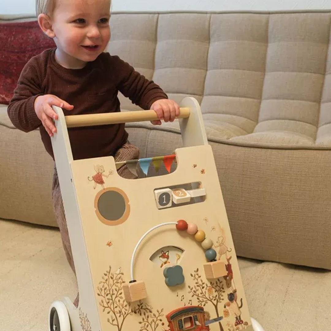 Een lachende baby staat achter de Egmont Toys houten activiteiten loopwagen en houdt de duwstang vast.