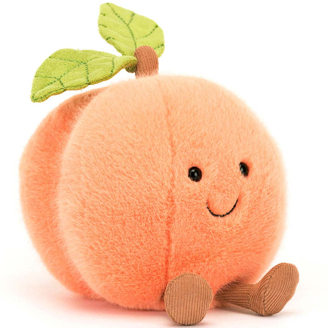 Jellycat knuffelperzik met lachend gezicht en groene blaadjes, schuin van voren gezien.