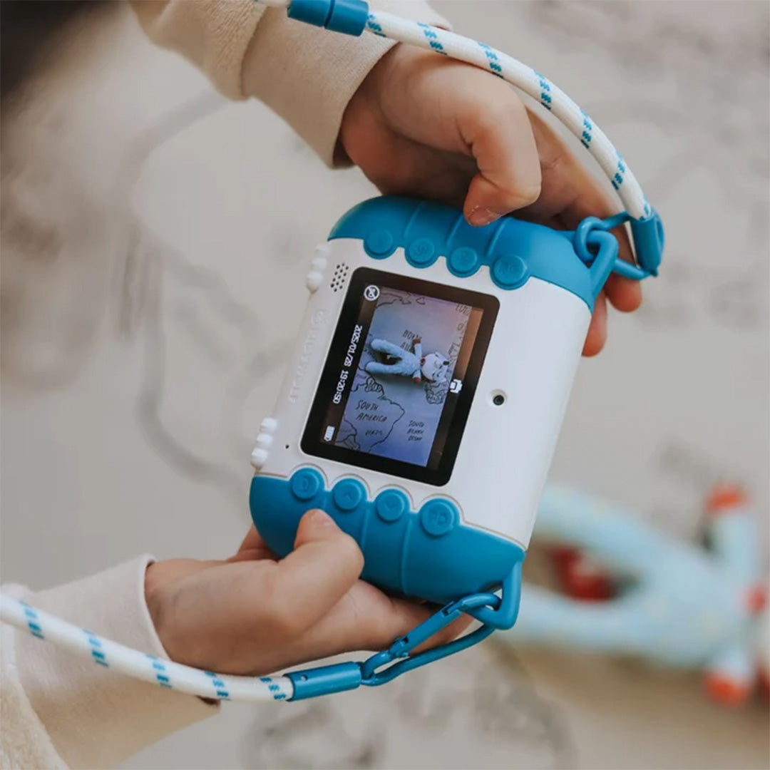 Kinderhanden houden de blauw-witte kidysnap kindercamera vast, met het scherm en de knoppen zichtbaar.