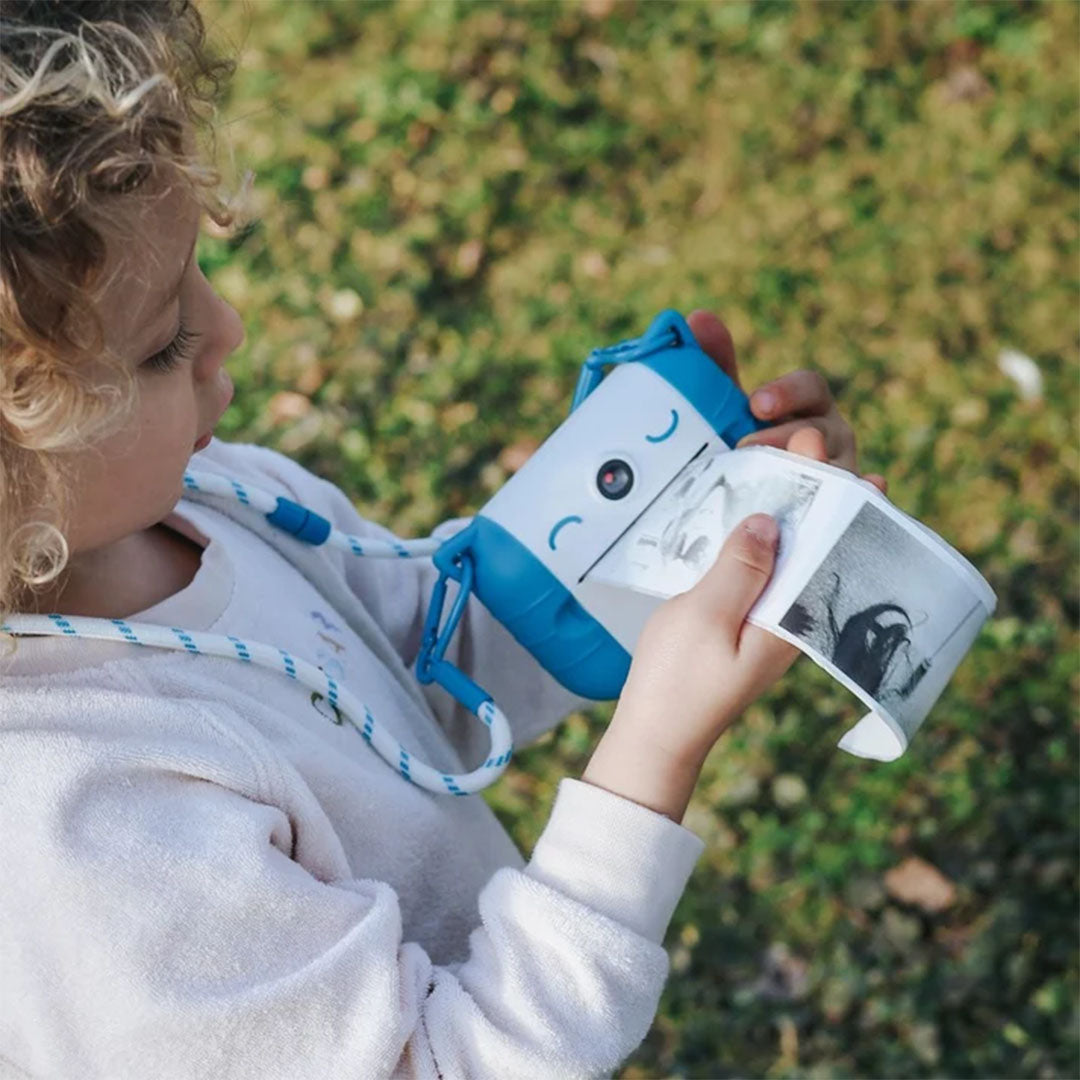 Een kind kijkt naar de blauw-witte kidysnap kindercamera terwijl deze een zwart-wit foto print.