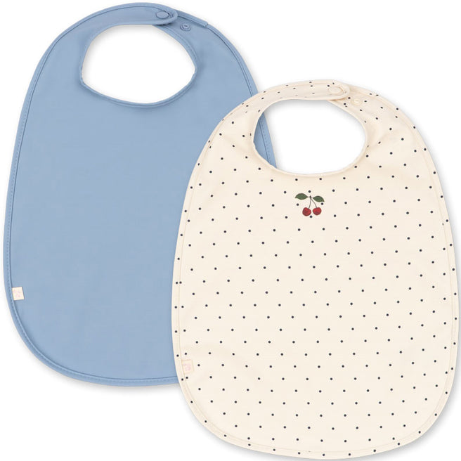 Konges Sløjd set van twee waterdichte babyslabjes, één lichtblauw en één crèmekleurig met stippen en kersen.