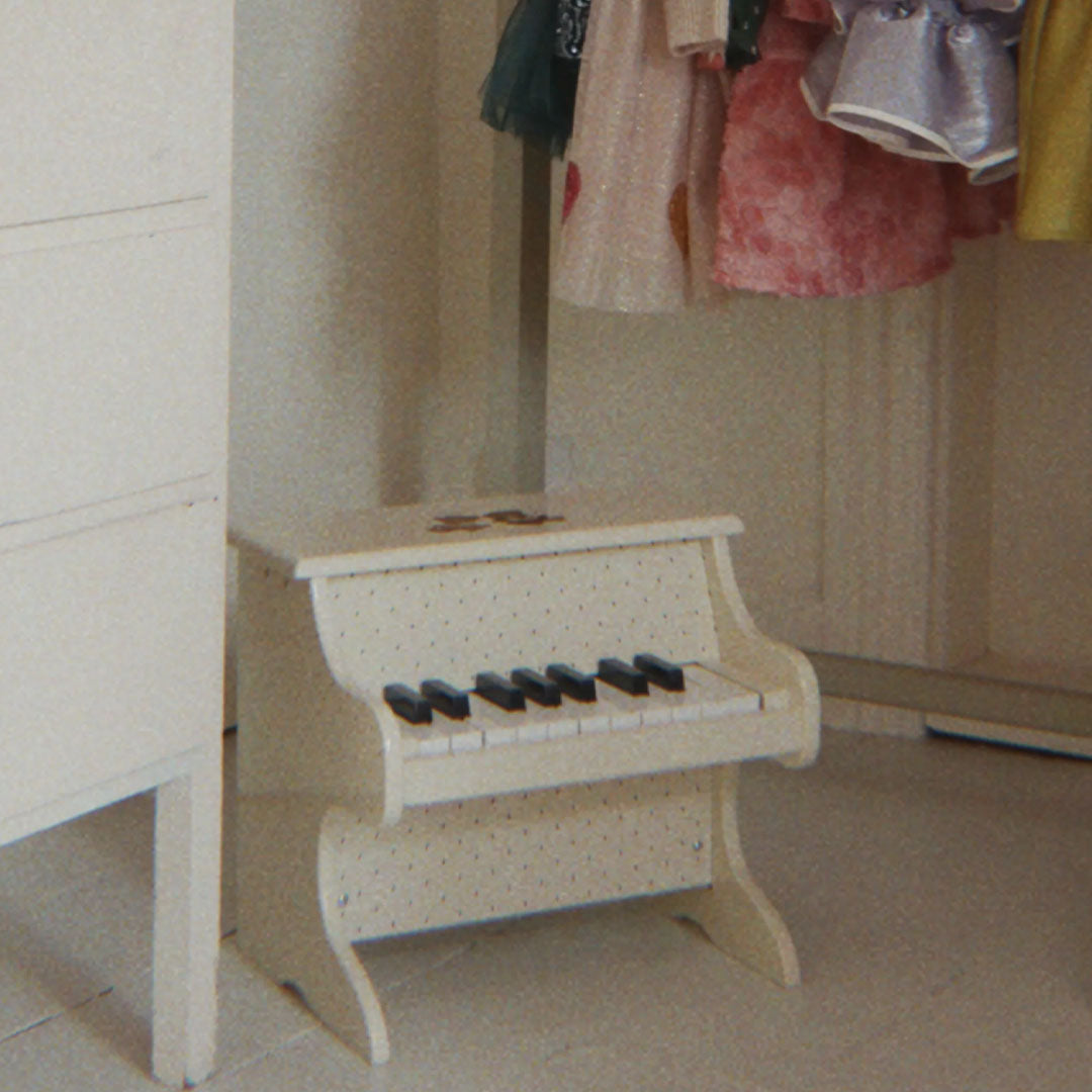 De beige houten speelgoedpiano staat in een kamer naast een kast.