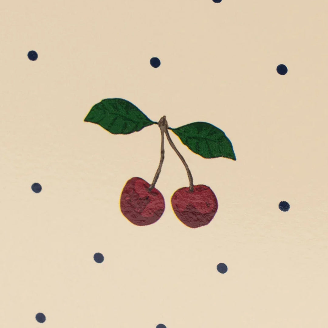 Detail van de kersenillustratie en zwarte stippen op het beige houten poppenbed.