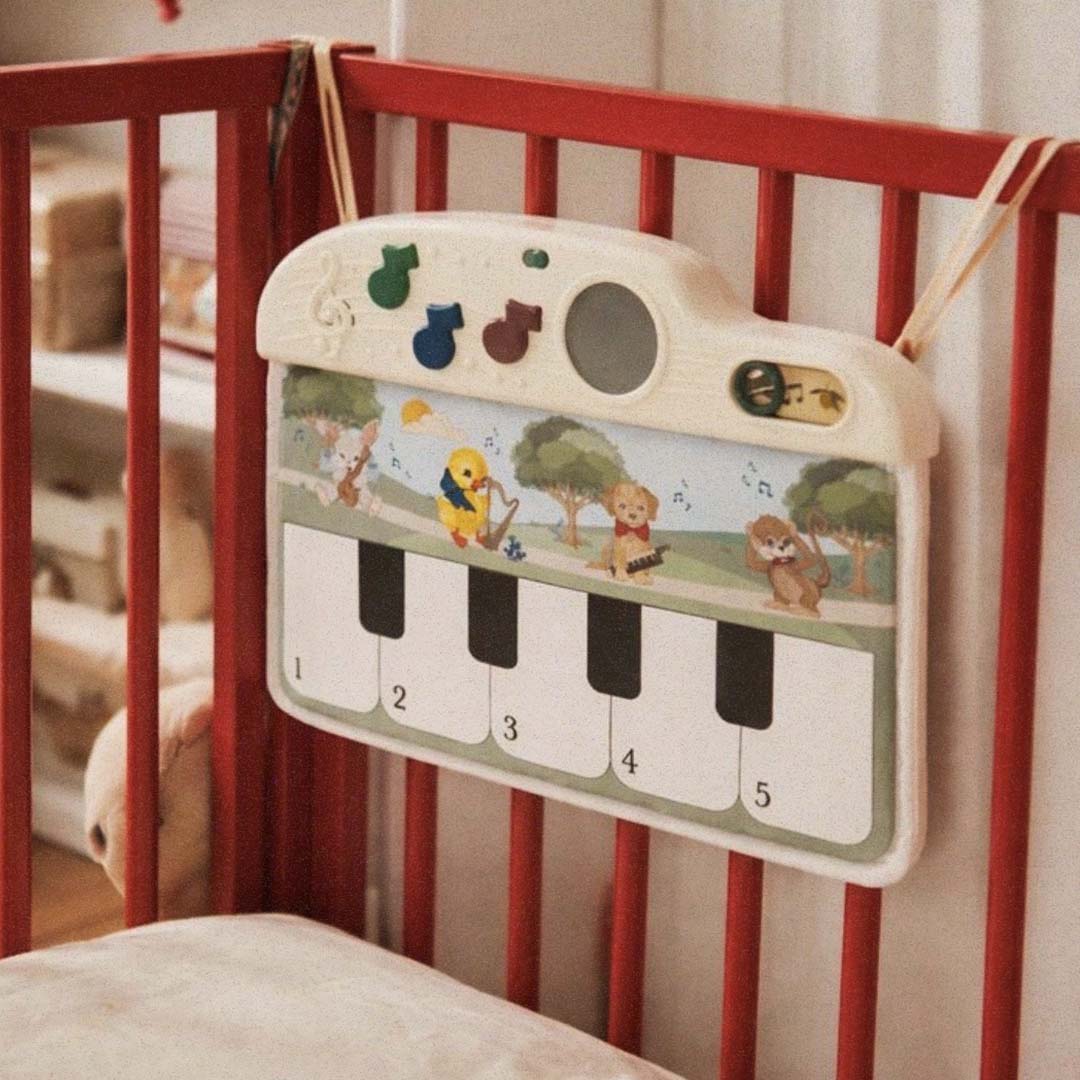 De Konges Sløjd muzikale activiteitenmat voor baby's hangt aan de rode spijlen van een ledikant.