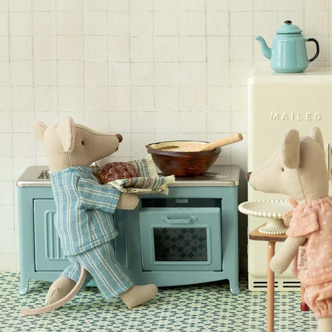 Twee Maileg muizen in pyjama bij de blauwe poppenhuis keuken, waarvan één een broodje uit de oven haalt.