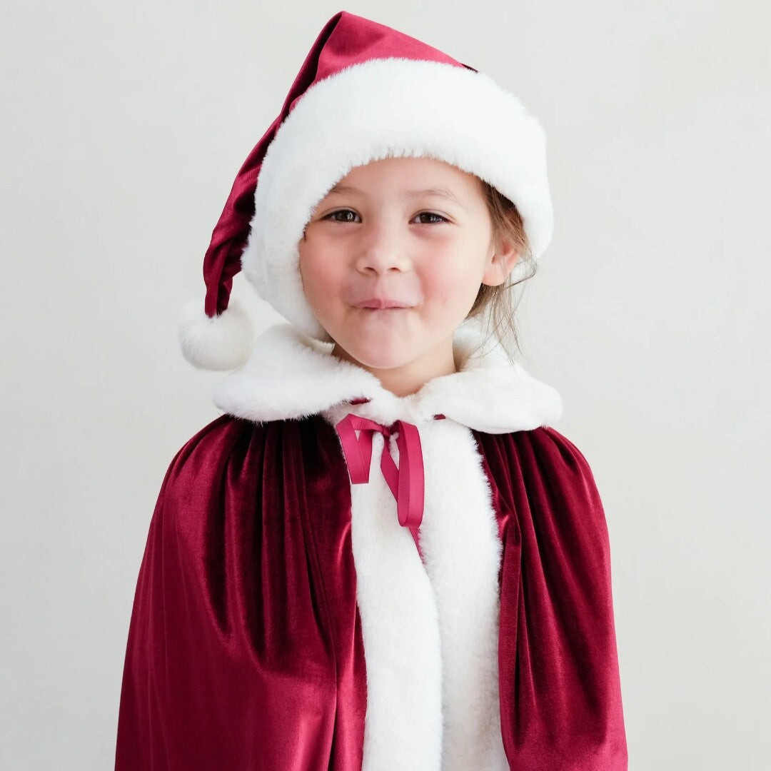 Meisje draagt een rode Kerst verkleedmuts en een bijpassende cape.