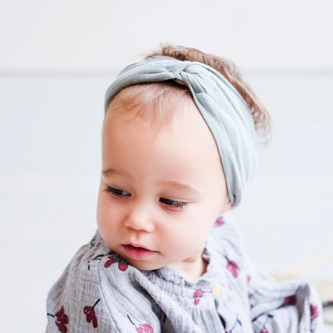 Een baby draagt de blauwe mimi & lula haarband met knoop.