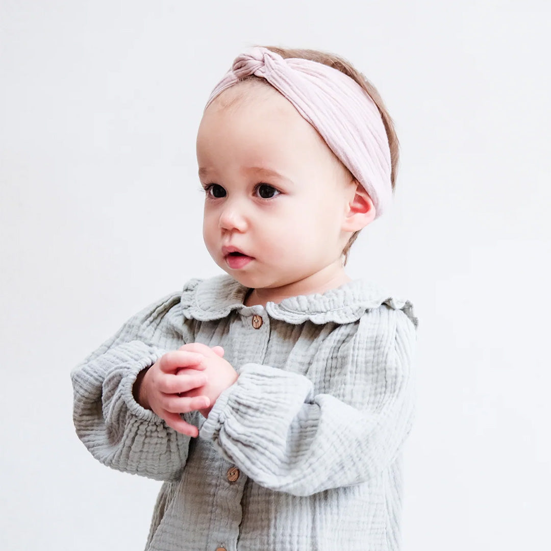 Een baby draagt de roze mimi & lula haarband met knoop.