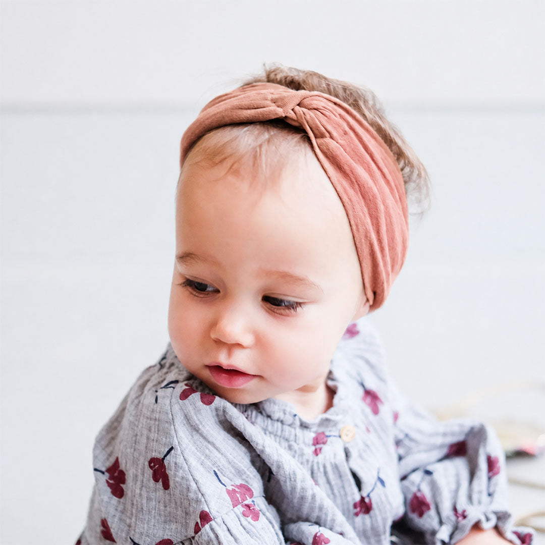 Een baby draagt de rustkleurige hoofdband met een knoop.