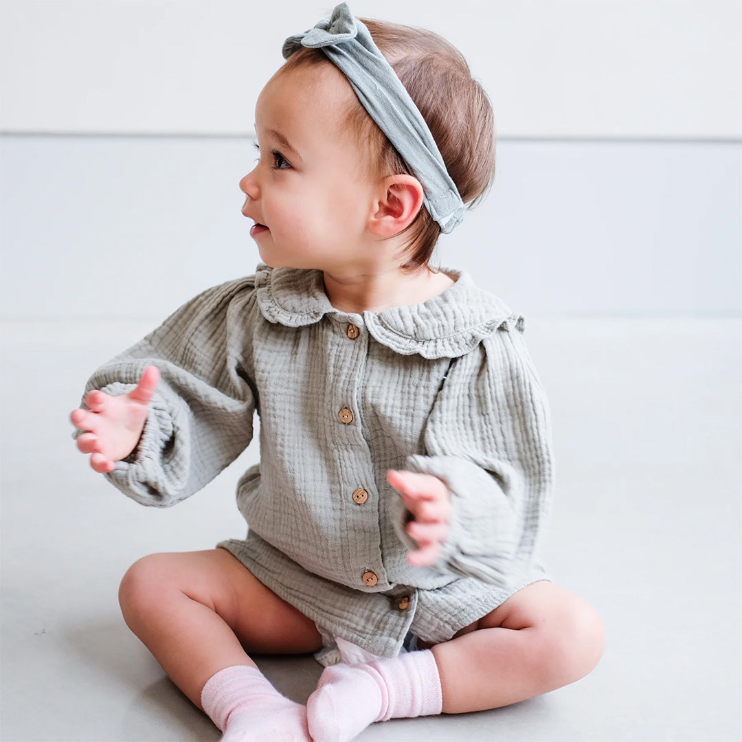 Baby draagt de Mimi & Lula gedempte blauwe haarband met strik, zittend en kijkend naar de zijkant.