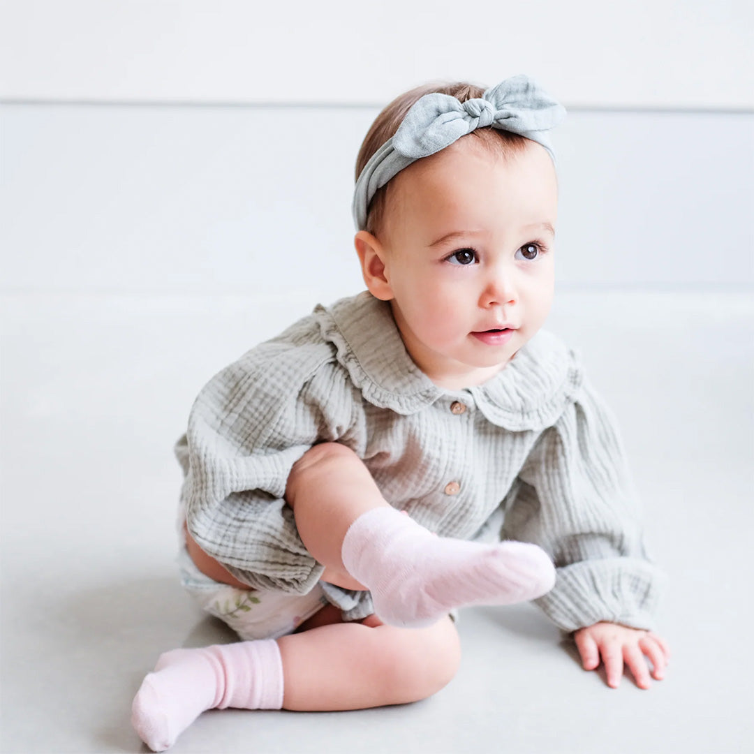 Baby draagt de Mimi & Lula gedempte blauwe haarband met strik, zittend en kijkend naar voren.