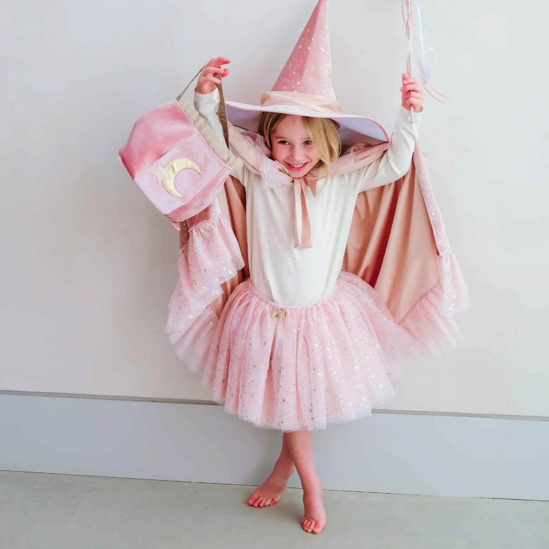 Lachend kind van voren met de mimi & lula roze heksenhoed, cape, tutu, toverstaf en tas met maan.