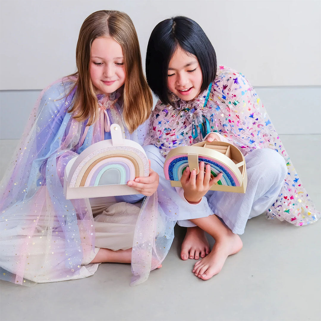 Twee meisjes zitten op de grond en houden elk een gesloten regenboog sieradendoosje vast.