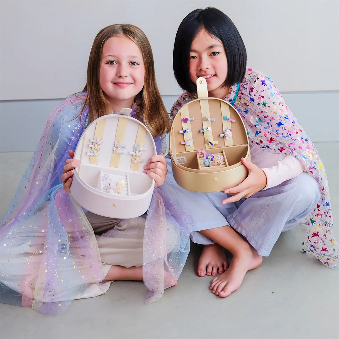 Twee lachende meisjes houden open regenboog sieradendoosjes vast, gevuld met haaraccessoires.