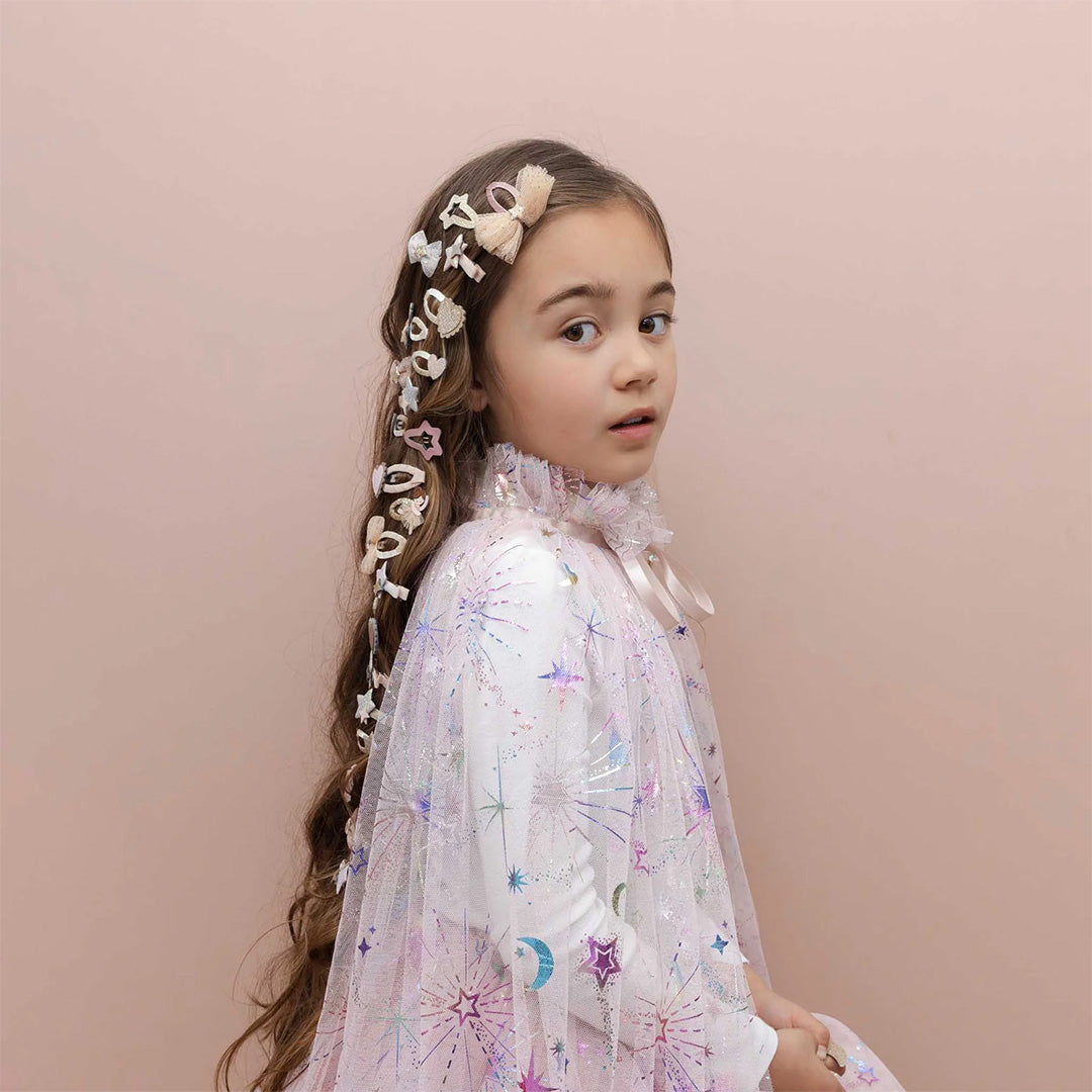 Een meisje met lang bruin haar draagt de mimi & lula roze verkleedcape met sterren en manen.