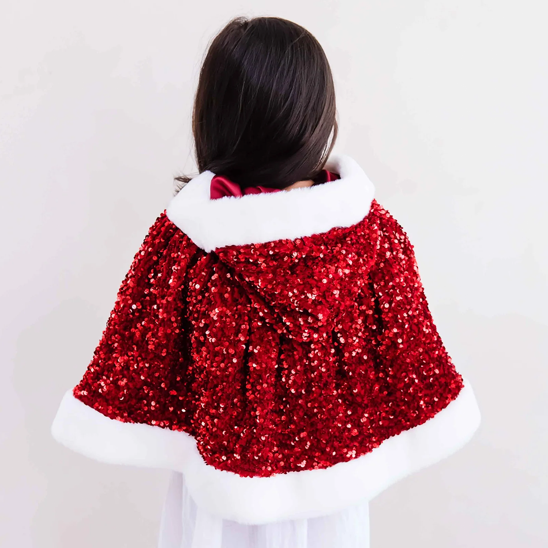 Meisje van achteren gezien draagt de mimi & lula rode Mrs Claus verkleedcape met pailletten en witte bontrand over een witte jurk.